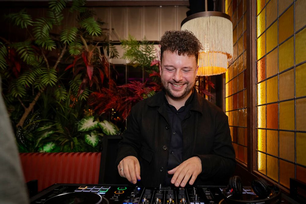 Een dj achter de draaitafel voor planten en amberkleurige glas-in-loodramen