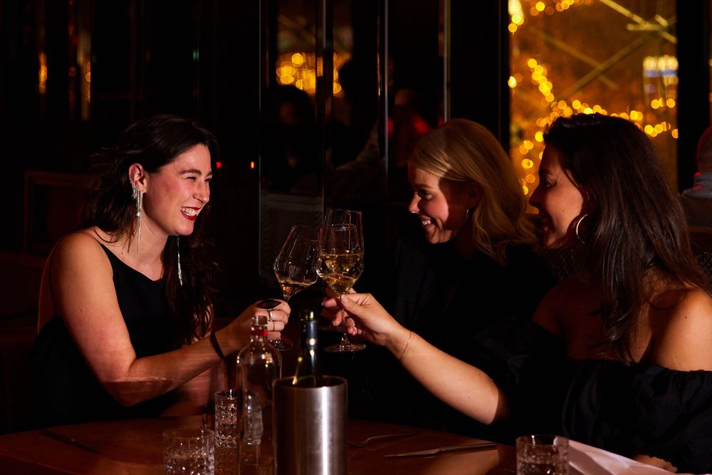 Drie vriendinnen proosten met witte wijn aan tafel op de eerste verdieping