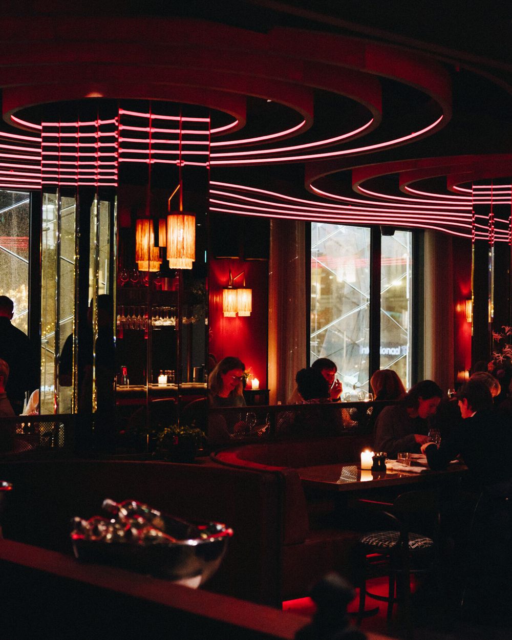 The dining room at night in red light under curved ceiling rings, with guests at the tables