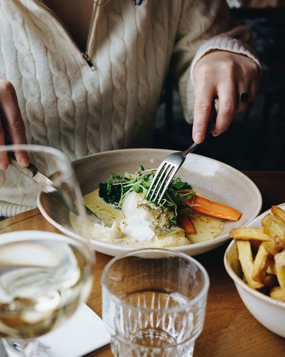 A guest eating a main course with a bowl of fries and a glass of white wine