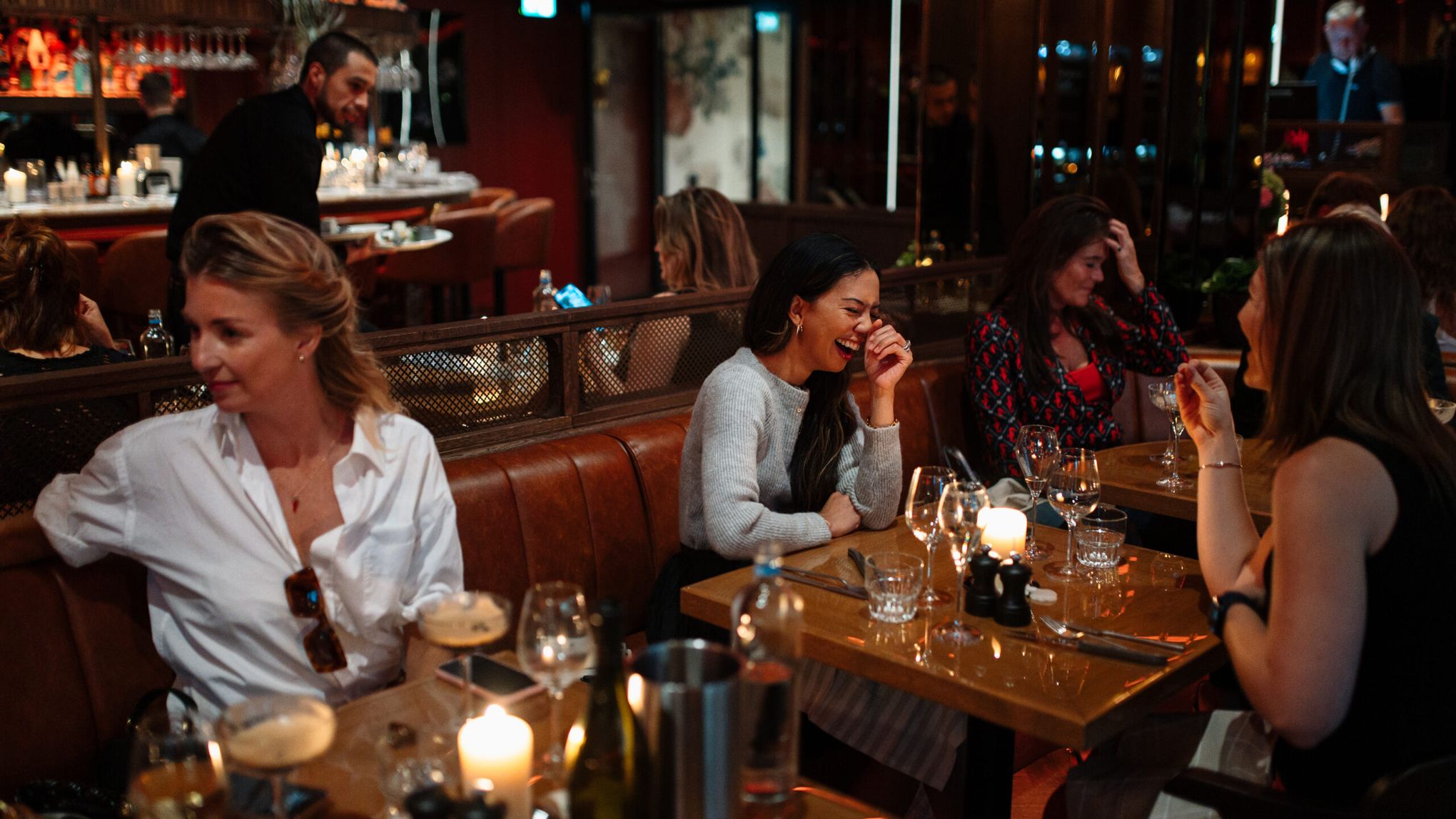 Vriendinnen lachen samen aan een tafel met kaarslicht in een leren zitbank