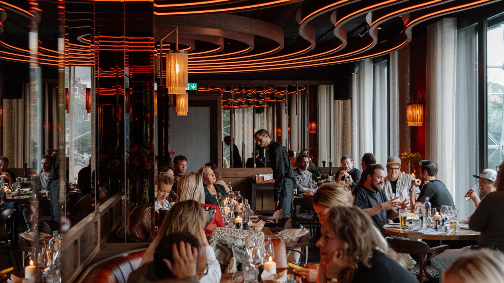 Gasten aan tafel in de Bistro onder het gebogen, verlichte plafond, met kaarsjes op tafel