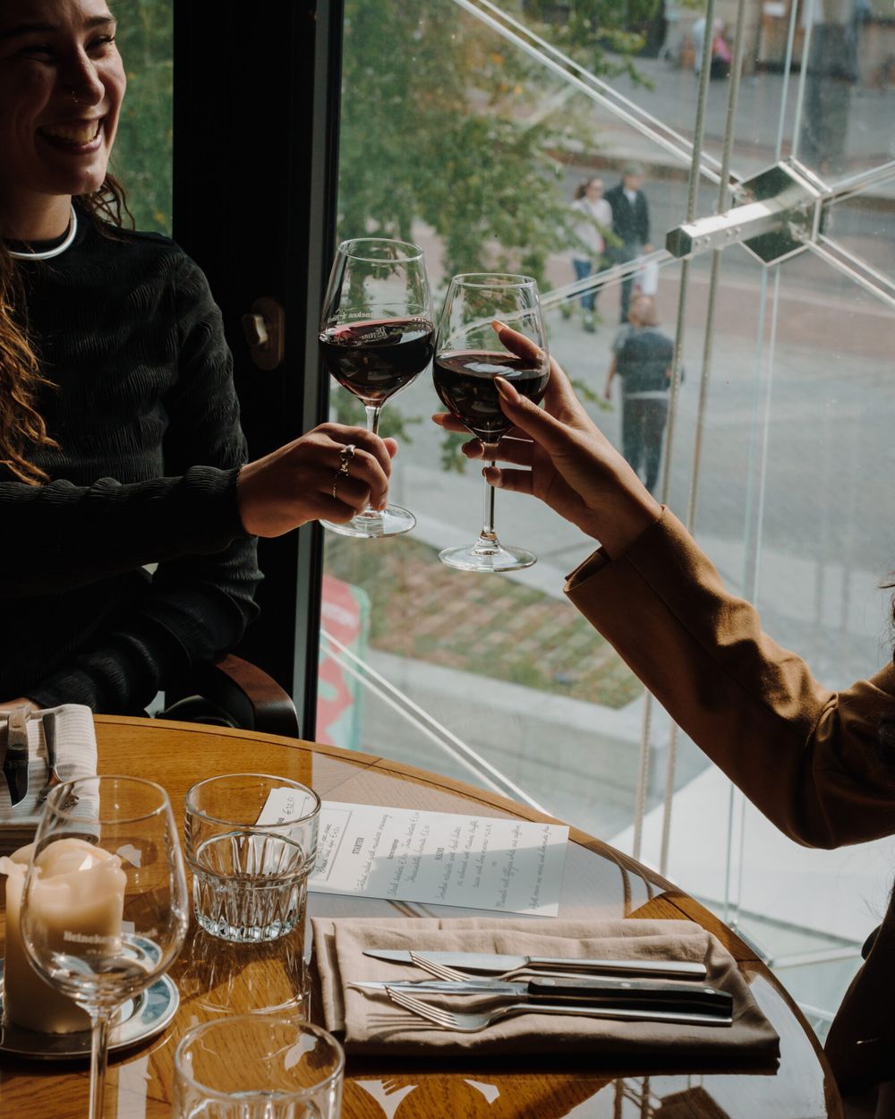 Two guests toasting with red wine at a table by the window