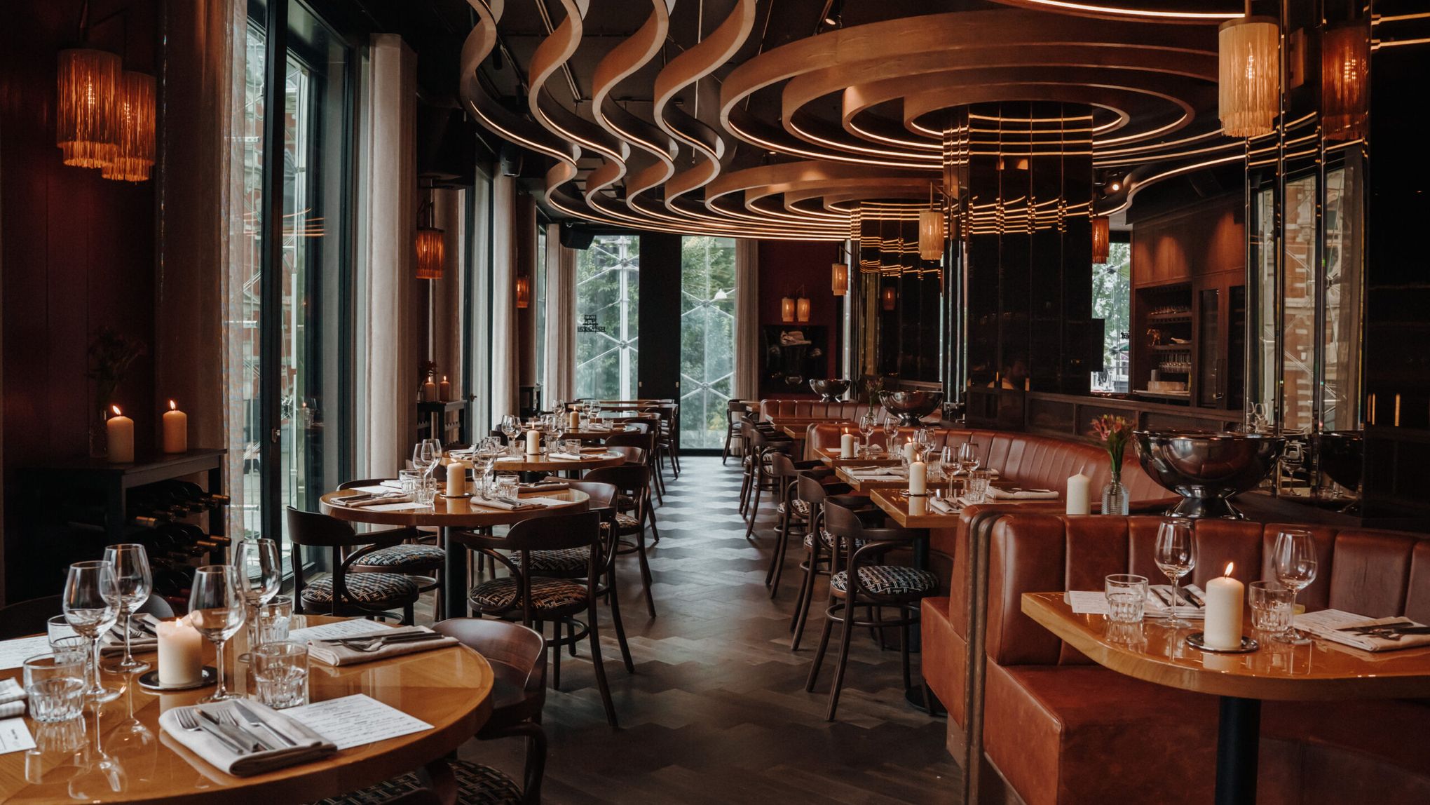 De eetzaal van de Bistro met gedekte tafels, leren banken, kaarsen en een gebogen verlicht plafond