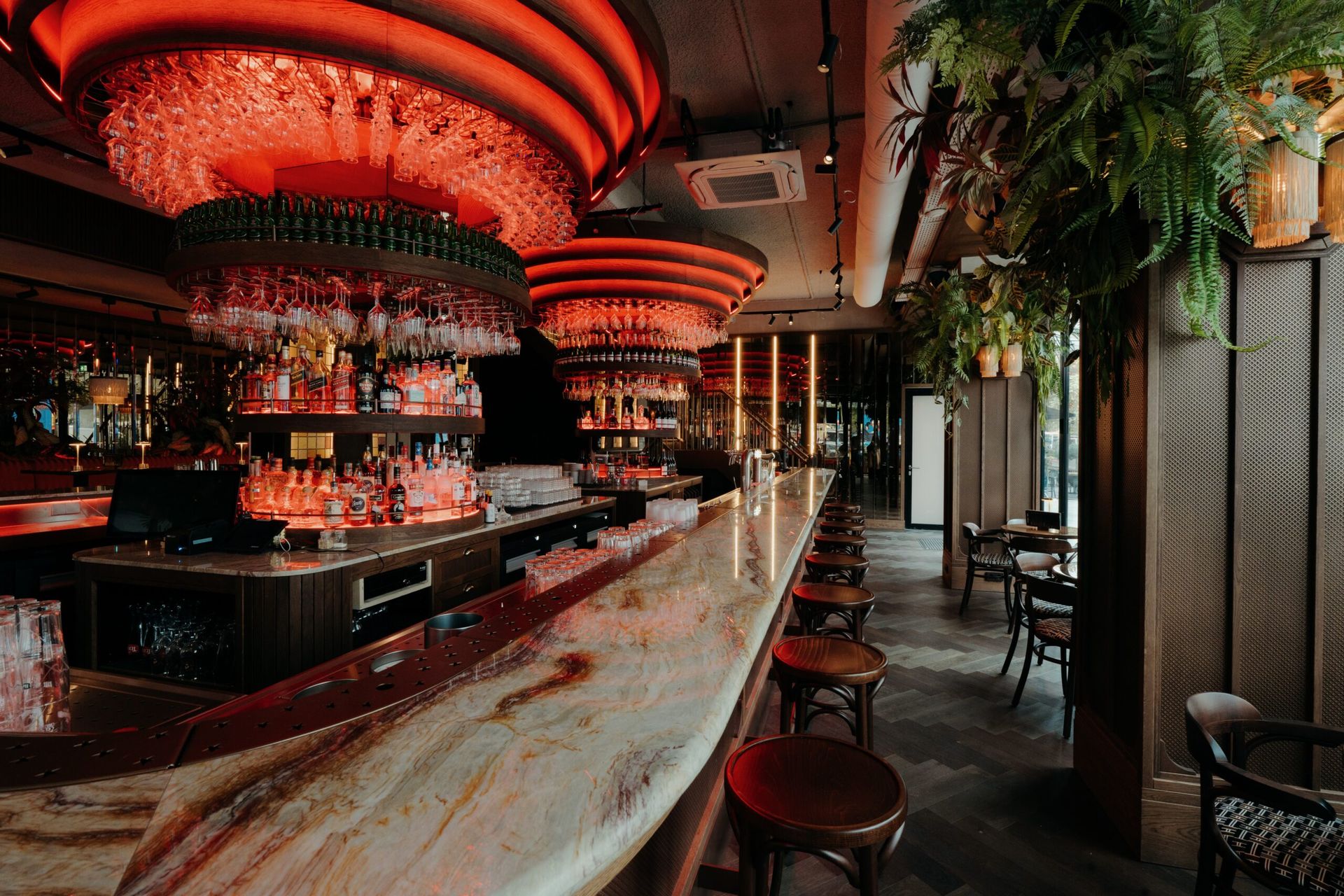 De bar van het Grand Café met de lange marmeren toog, houten barkrukken en ronde glazenrekken in rood licht