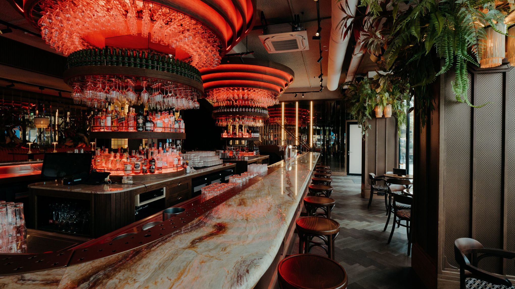 De bar van het Grand Café met de lange marmeren toog, houten barkrukken en ronde glazenrekken in rood licht
