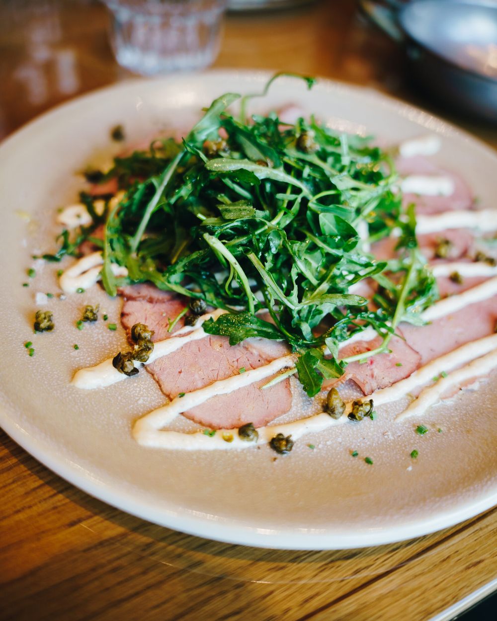 Thinly sliced meat with a creamy sauce, rocket and crispy capers on a light plate
