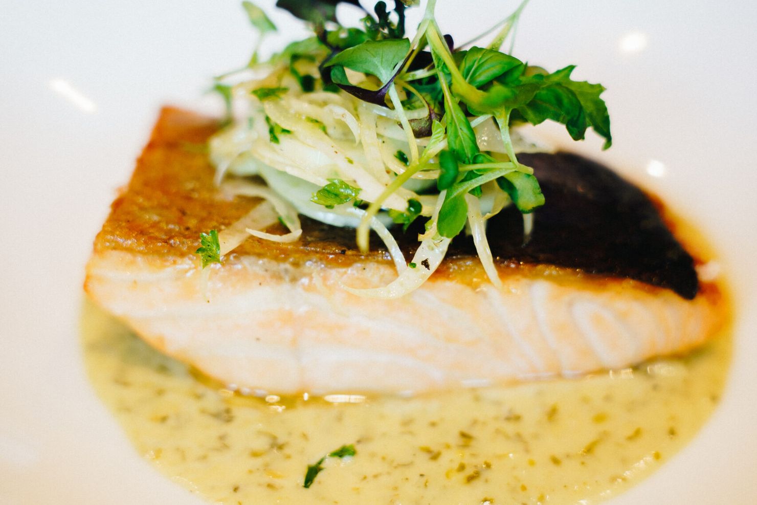 Crispy-skinned salmon fillet topped with fennel and cress in a herb sauce