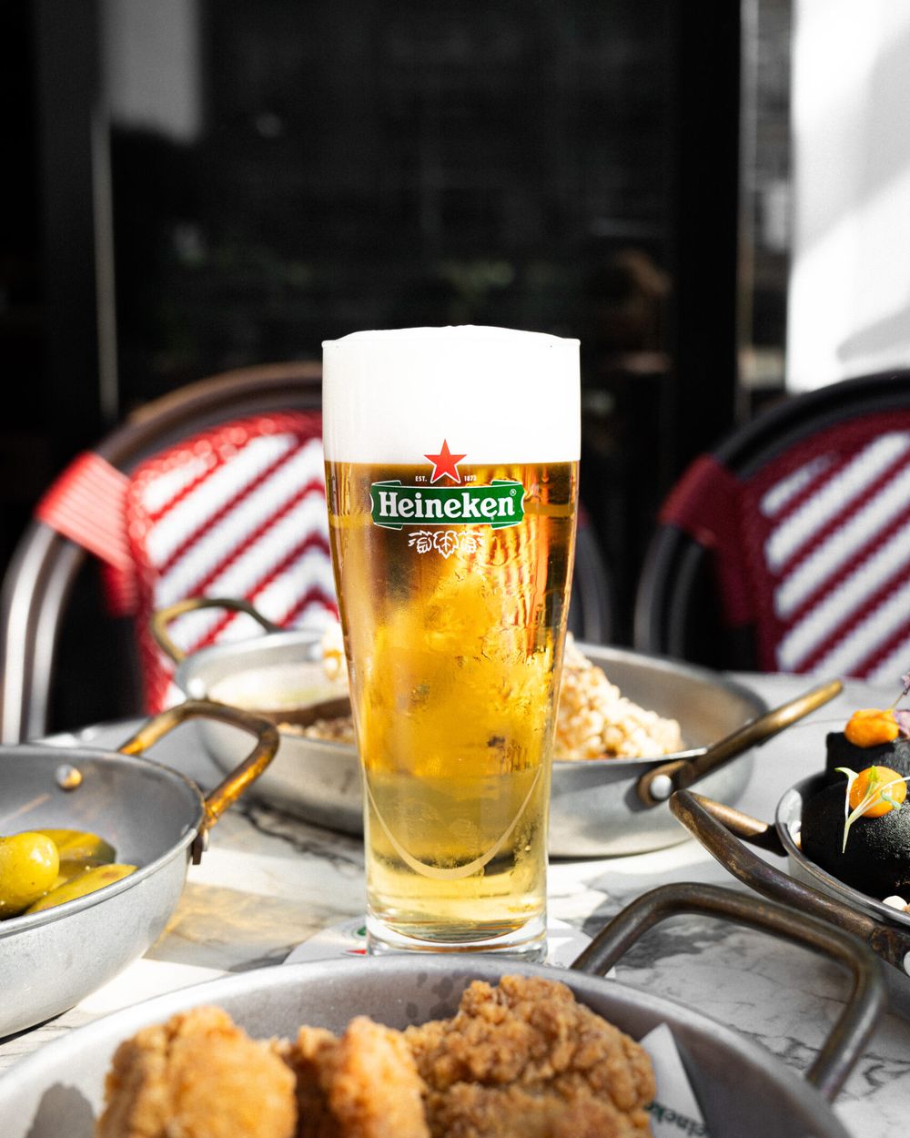 Een glas Heineken op een marmeren tafel tussen borrelhapjes: gefrituurde kip, olijven en kroketjes